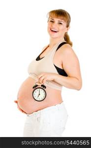 Happy pregnant woman holding alarm clock in front of her belly isolated on white&#xA;