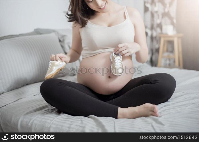 Happy pregnant woman holding baby shoes