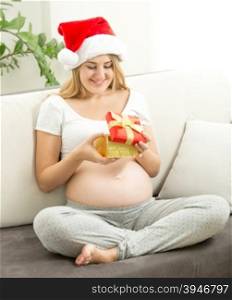 Happy pregnant woman in Santa cap looking inside of gift box
