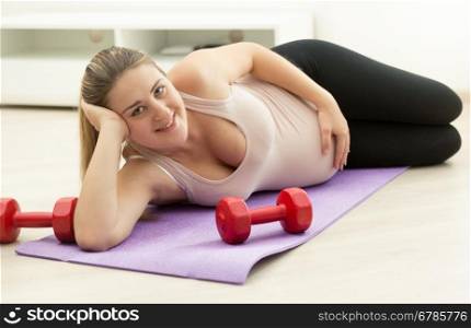 Happy pregnant woman relaxing on fitness mat after exercising