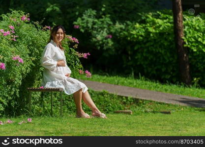 happy pregnant woman sitting on bench in the park 