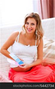 Happy pregnant woman sitting on couch with paint samples&#xA;