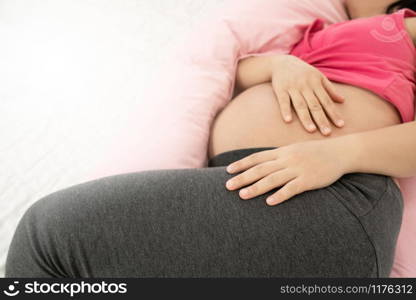 Happy pregnant woman sleeping on bed in bedroom at home for resting and stress relief. The young expecting mother holding baby in pregnant belly. Maternity prenatal care and woman pregnancy concept.. Happy pregnant woman sleeping on bed in bedroom.