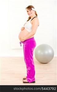 Happy pregnant woman standing on weight scale and holding her belly&#xA;