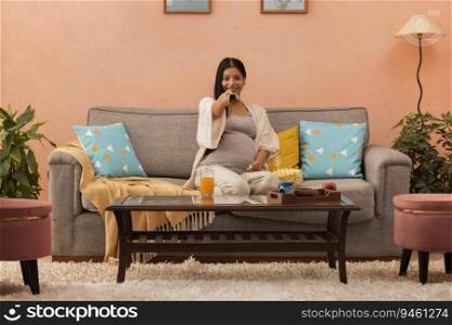 Happy pregnant woman watching TV in living room