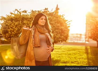 Happy pregnant woman with shopping bag in bright sunny day on the backyard, preparing to baby birth, enjoying last days of pregnancy