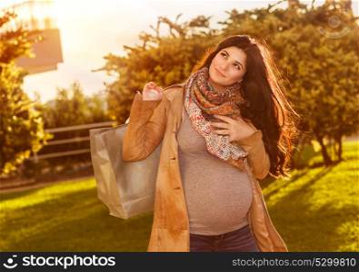 Happy pregnant woman with shopping bag in sunny autumn day on the backyard, preparing to baby birth, enjoying last days of pregnancy