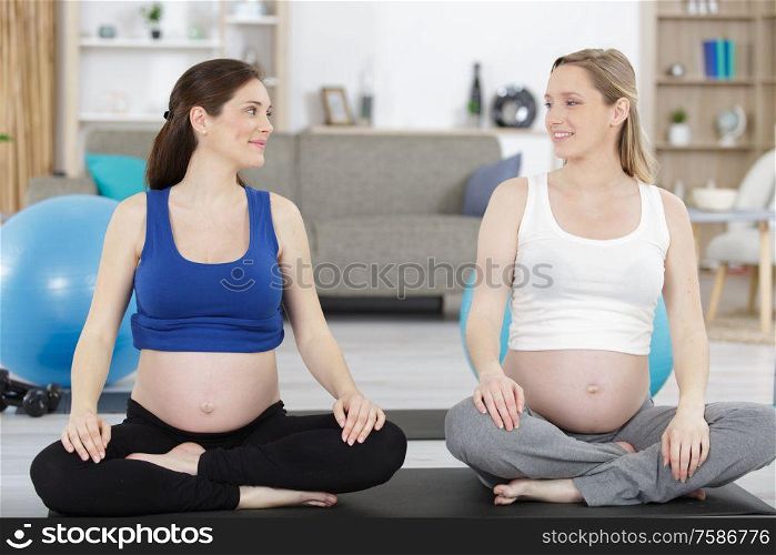 happy pregnant women sitting and talking on mats in gym