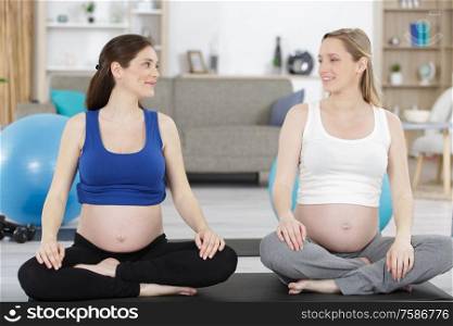 happy pregnant women sitting and talking on mats in gym