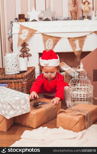 Happy pretty baby dressed in costume Santa Claus with Christmas gifts. Festive Christmas decoration