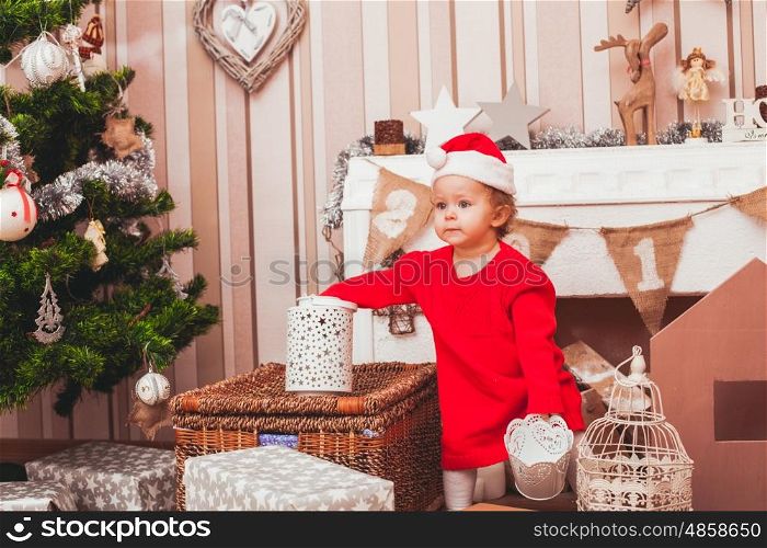 Happy pretty baby dressed in costume Santa Claus with Christmas gifts. Festive Christmas decoration