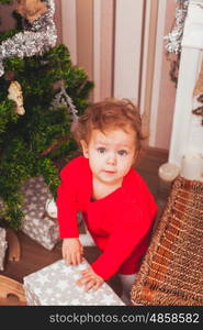 Happy pretty baby dressed in red dress with Christmas gifts. Festive Christmas decoration