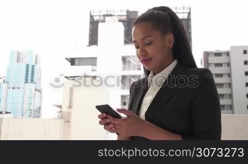 Happy pretty black female manager using phone. Portrait of young businesswoman, successful girl, busy woman at work, texting with smartphone, text messaging on mobile telephone near office building