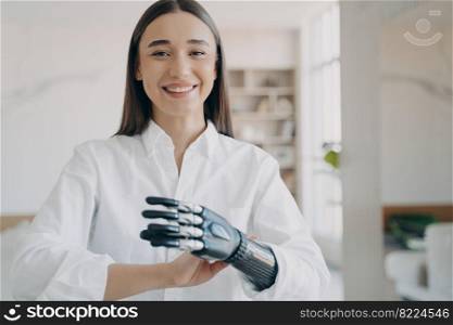 Happy pretty disabled girl enjoying using bionic prosthetic arm at home. Smiling young woman satisfied with artificial limb, high tech prosthesis. Lifestyle of people with disabilities.. Happy disabled girl enjoy using bionic prosthetic arm, high tech artificial limb, standing at home