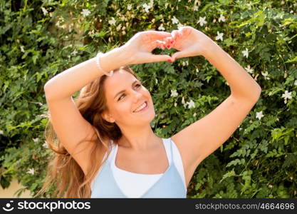 Happy pretty girl on a sunny day in the park making a heart with her hands