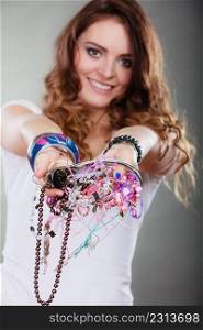 Happy pretty young woman wearing bracelets and rings holding many plentiful of precious jewelry necklaces beads. Portrait of gorgeous fashion girl in studio on gray.. Happy woman with jewelry necklaces ring bracelets