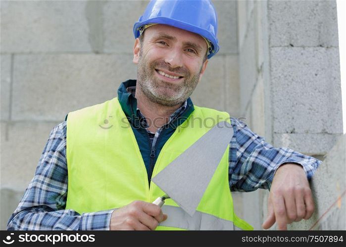 happy professional builder in the helmet is plastering the wall