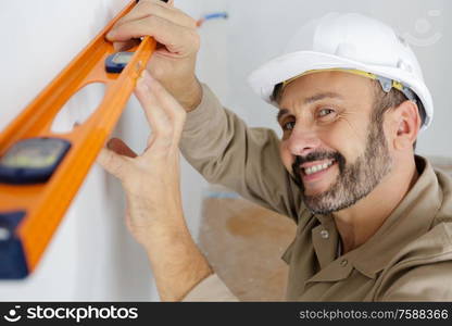 happy professional worker in helmet is measuring wall with level