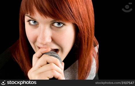 Happy redhead girl singing karaoke on a microphone. Studio shot.