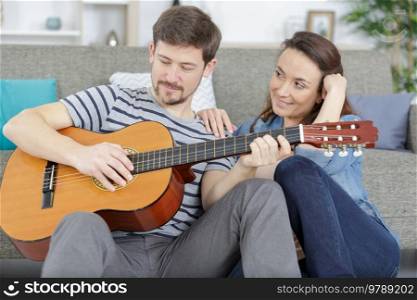 happy relaxed couple with guitar sitting on couch at home