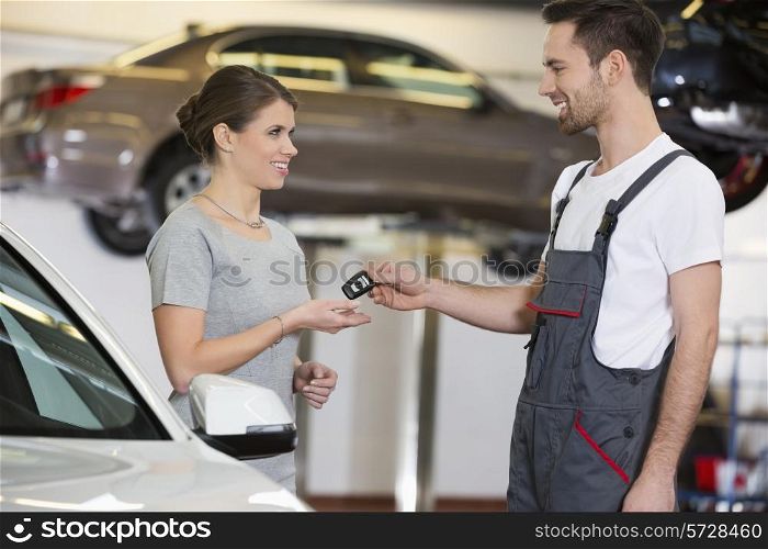 Happy repairman giving car key to woman in workshop