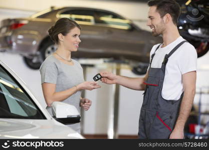 Happy repairman giving car key to woman in workshop