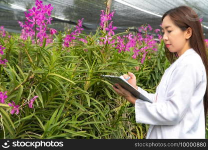 Happy researcher botanical research orchid wearing a white cap and her hand holding a pen and notebook for taking notes for research