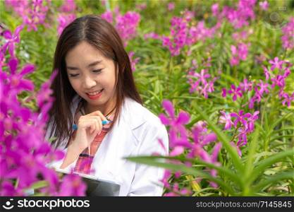 Happy researcher botanical research orchid wearing a white cap and her hand holding a pen and notebook for taking notes for research
