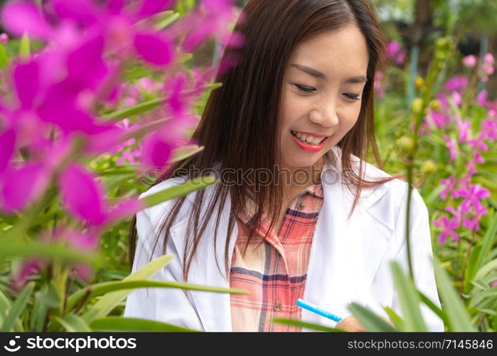 Happy researcher botanical research orchid wearing a white cap and her hand holding a pen and notebook for taking notes for research