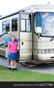 Happy retired couple standing beside their luxury motor home.