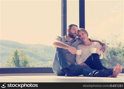 happy romantic couple enjoying morning coffee on the floor by the window in their luxury home. romantic couple enjoying morning coffee
