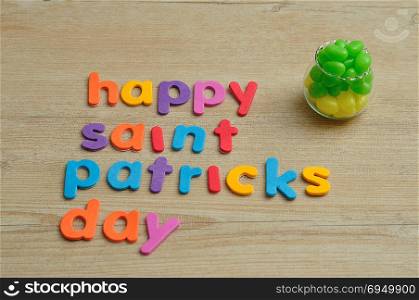Happy saint Patricks day in colorful letters on a wooden background with a pot filled with green and yellow jelly beans
