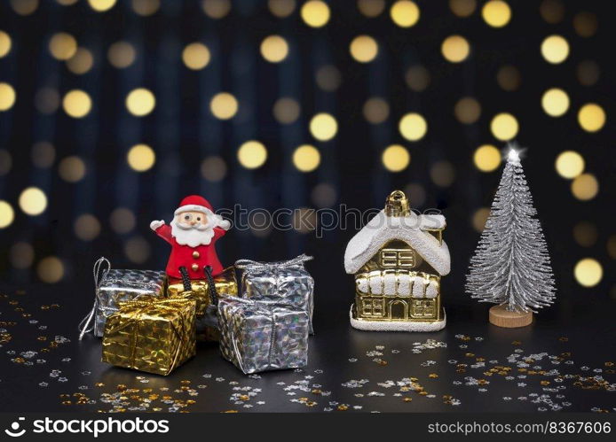 Happy Santa Claus doll sitting on gift boxes with Christmas decorations on blurred hanging decorative lights in night background