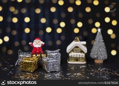 Happy Santa Claus doll sitting on gift boxes with Christmas decorations on blurred hanging decorative lights in night background