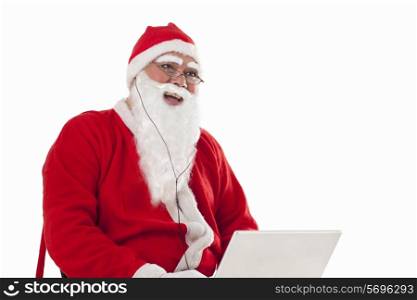 Happy Santa Claus listening to music while using laptop over white background