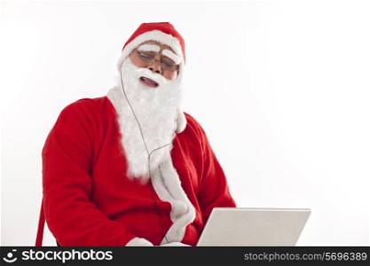 Happy Santa Claus listening to music with eyes closed with laptop over white background