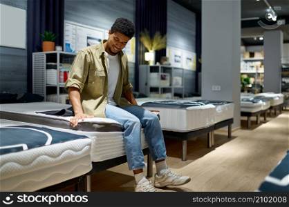 Happy satisfied man choosing examining orthopedic mattress in furniture store sitting on soft bed. Man choosing mattress sitting on shop bed