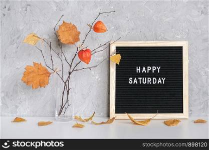 Happy Saturday text on black letter board and bouquet of branches with yellow leaves on clothespins in vase on table Template for postcard, greeting card Concept Hello autumn Saturday.. Happy Saturday text on black letter board and bouquet of branches with yellow leaves on clothespins in vase on table Template for postcard, greeting card Concept Hello autumn Saturday