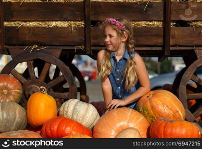 Happy school girl sitting between pumpkins at local farmer market in sunny autumn day.. Happy school girl sitting between pumpkins at local farmer market in sunny autumn day