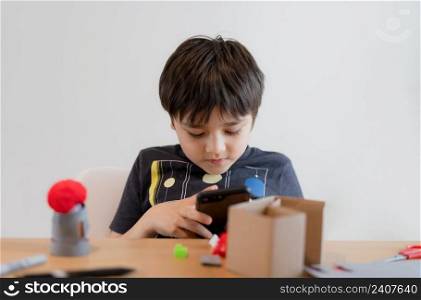 Happy schoolkid making DIY Easter decorations homework and using mobile phone sending to the  teacher, Child boy preparing and getting ready for Easter hunt  for celebration on School holiday 