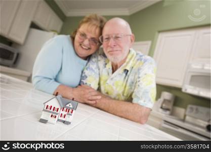 Happy Senior Adult Couple Gazing Over Small Model Home on Their Kitchen Counter.