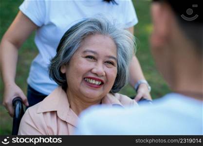 Happy senior Asian grandmother uses wheelchair with her daughter and grandchild in park, Grandson came to visit elderly grandmother and hold hand. Concept of happy family, good relationship together