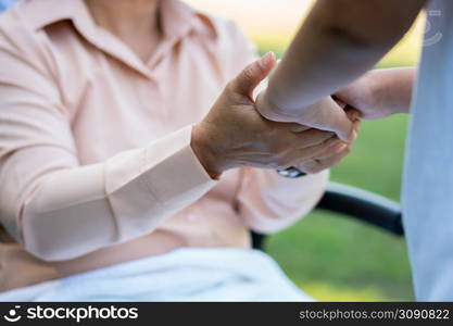 Happy senior Asian grandmother uses wheelchair with her daughter and grandchild in park, Grandson came to visit elderly grandmother and hold hand. Concept of happy family, good relationship together