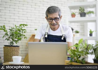 happy senior asian retired man with laptop is relaxing and enjoying leisure activity in garden at home.