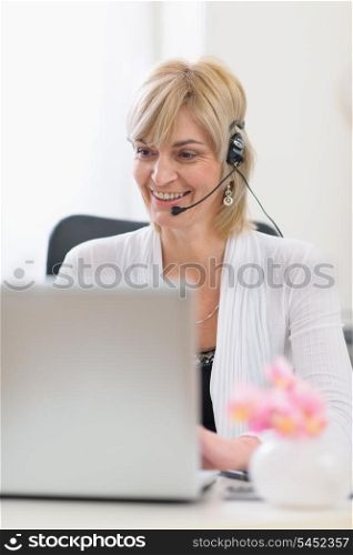 Happy senior business woman with headset working on laptop
