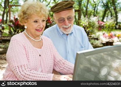 Happy senior couple on their laptop computer in a beautiful outdoor setting.