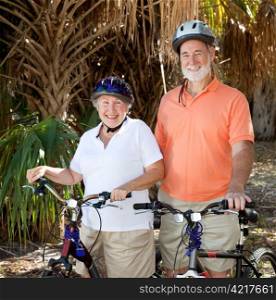 Happy senior couple riding their bikes with helmets on.