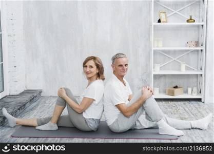 happy senior couple sitting back back grey yoga mat