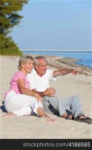Happy Senior Couple Sitting Pointing on Beach