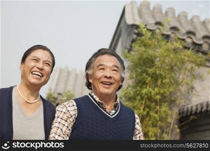 Happy senior couple walking outdoors by traditional building in Beijing